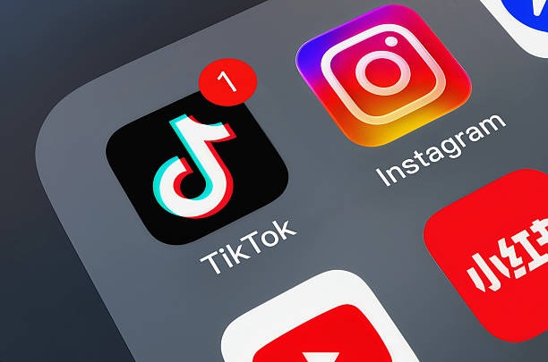 A close-up shot of a smartphone screen showing social media app icons, featuring TikTok with a red notification badge, Instagram, and YouTube on a dark grey background.